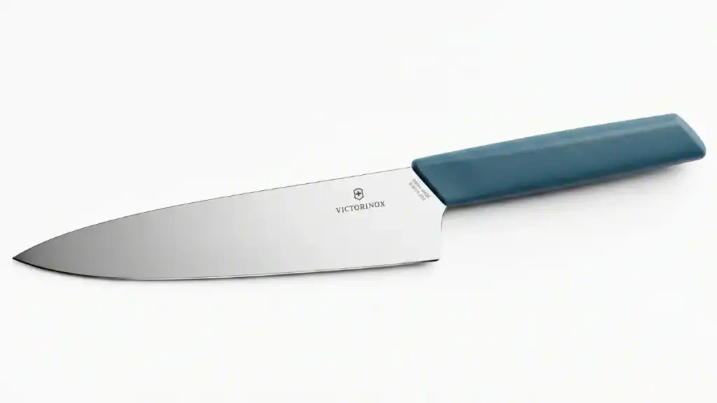 Tramontina Century vs Victorinox: Comparação visual de duas facas de chef de 8 polegadas, sendo a Tramontina forjada com rebites (esquerda) e a Victorinox estampada (direita), sobre uma tábua de madeira.
